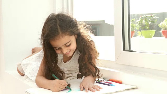 年轻女孩坐在家里的窗台上用彩色蜡笔给图画上色，印度德里视频素材