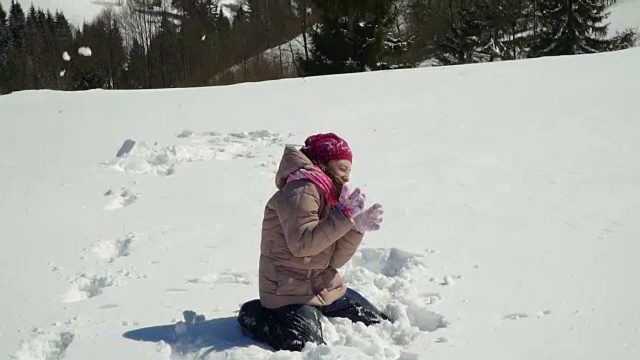一个快乐的小女孩正在抛雪。她是笑。一个女孩在大自然的深山冬林里散步。缓慢的运动。视频下载
