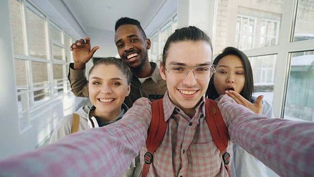 四个积极开朗、有吸引力的多民族朋友在大学走廊里拿着智能手机自拍，玩得很开心视频下载