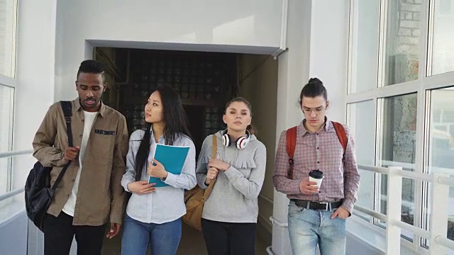四个严重集中的不同种族的男女学生走在白色宽敞的大学走廊复习材料考试前视频素材