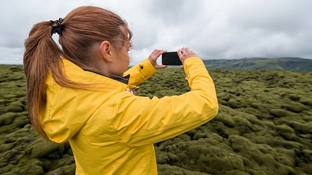 身着黄色雨衣的女子正在拍摄覆盖着苔藓的熔岩地视频素材