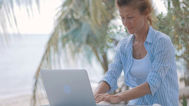 一个年轻女子坐在桌子旁，手提电脑后面是海景视频素材