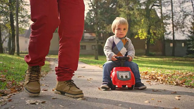 SLO MO蹒跚学步的孩子在一个阳光明媚的日子里和他的爸爸在公园里骑着他的三轮车视频素材