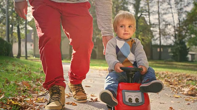 SLO MO蹒跚学步的孩子坐在三轮车上，被他的爸爸推着向前走视频素材