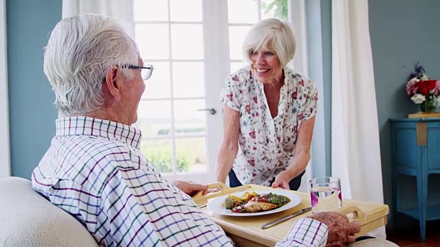 年长的女人给坐在家里的年长的男人上菜视频素材