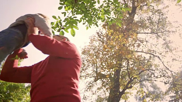 爷爷抱着蹒跚学步的孙子在阳光明媚的公园里打转视频素材
