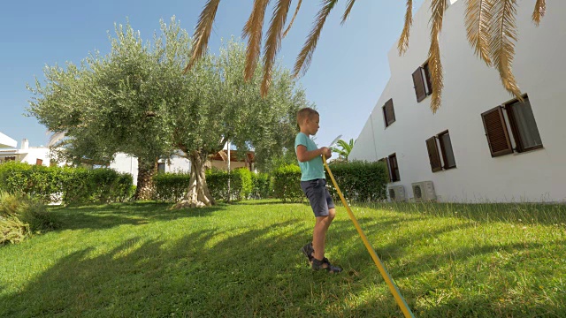 孩子负责给房子旁边的绿草坪浇水视频素材