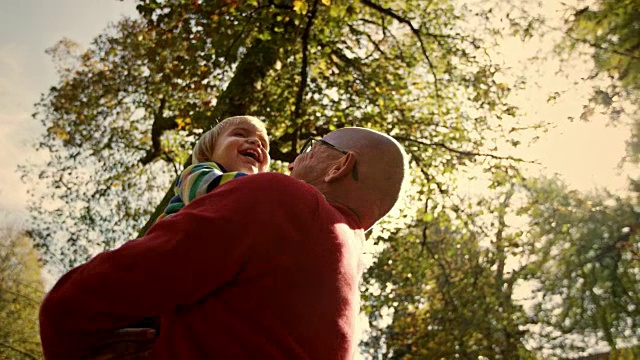 SLO MO Man在阳光明媚的公园里抱着他的孙子，亲吻着他笑着的孙子视频素材