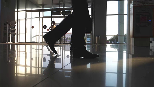 两个不认识的商人的脚在机场候机楼。年轻商人的双腿走到一起。同事在室内。慢动作低角度视角特写视频素材