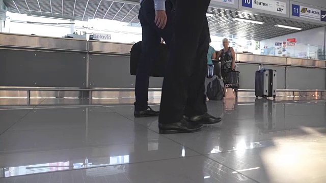 两个不认识的商人的脚在机场候机楼。年轻商人的双腿走到一起。同事在室内。慢动作低角度视角特写视频素材