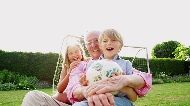 爷爷和孙子坐在花园里踢足球视频素材
