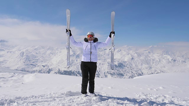 快乐的女人在山顶上举起她的下坡滑雪板视频素材