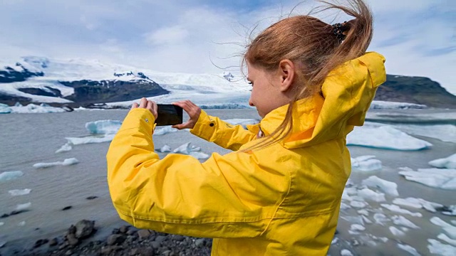 在一个刮风的日子里，一名妇女在冰川泻湖上拍摄漂浮的冰山视频下载