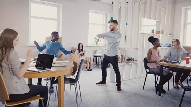 年轻快乐的商人跳着胜利的舞蹈，与混血员工在现代4K办公室庆祝团队成功视频素材