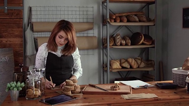一位女士正在为她在面包店制作的新鲜面包写配料视频素材
