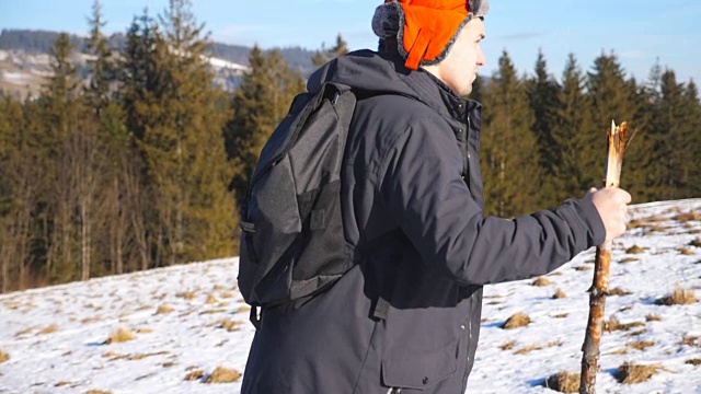 侧面的年轻徒步旅行者与背包和手在雪山上攀登在田野。运动的家伙在阳光明媚的雪地上徒步旅行。健康积极的生活方式。冬季森林的背景。慢镜头视频素材