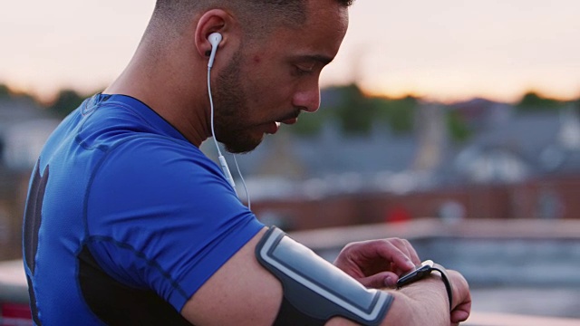 男性跑步者在街道上设置智能手表上的应用程序，开始跑步视频素材