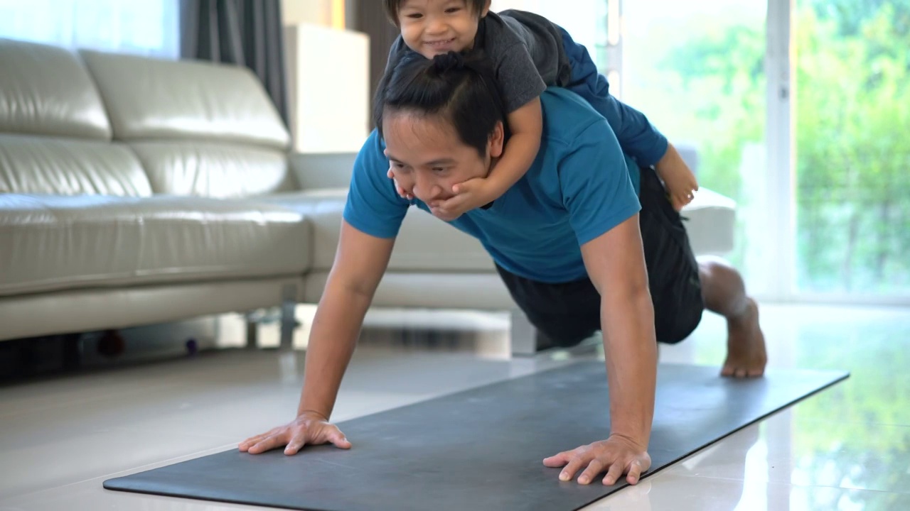 一个男人在家里背着开心的宝宝做俯卧撑。视频下载