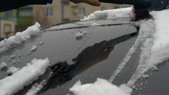 慢动作拍摄手从结冰的汽车挡风玻璃上刮雪，雪花在阳光下流动视频素材