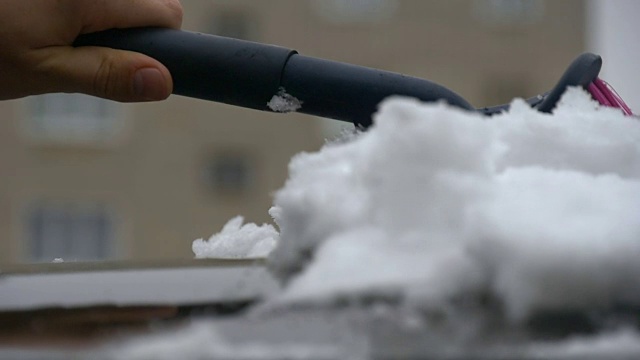 慢动作拍摄手从结冰的汽车挡风玻璃上刮雪，雪花在阳光下流动视频素材