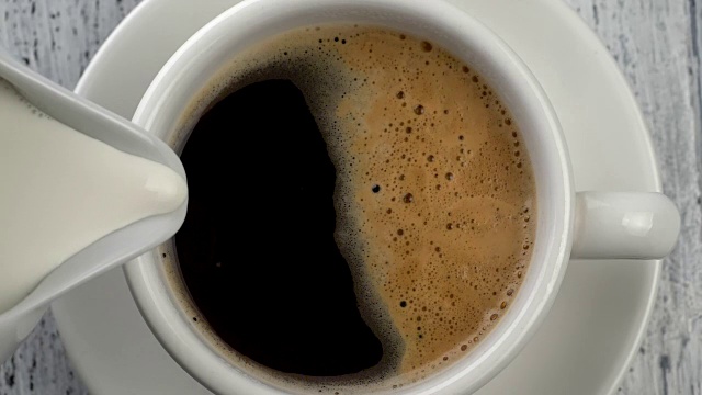 把牛奶倒进咖啡杯。复古的白色木制背景。自顶向下。慢动作镜头视频素材