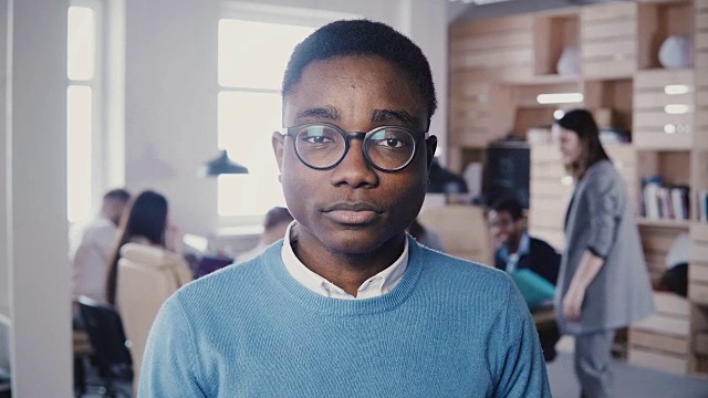 年轻的非洲裔办公室职员戴着眼镜盯着镜头。时尚的平面设计师摆姿势和微笑4K视频素材