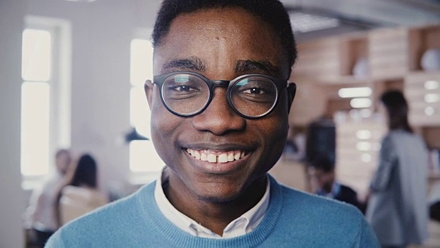 不可思议的近距离肖像英俊的年轻非洲裔美国人戴眼镜微笑在繁忙的办公室4K相机视频素材