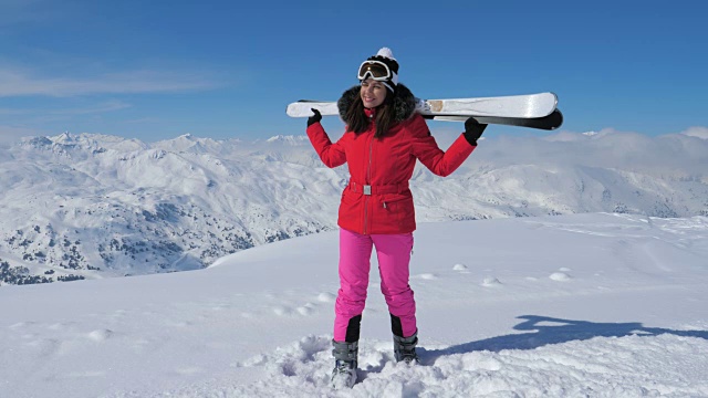 女子滑雪者站在山坡上，手握滑雪板放在肩膀上视频素材