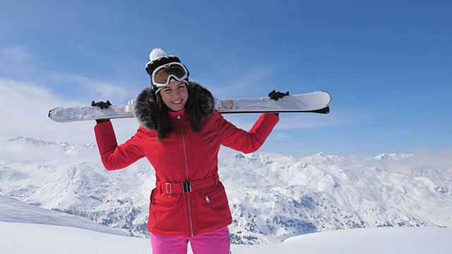 微笑的漂亮女子滑雪者站在山坡上，肩上扛着滑雪板视频素材