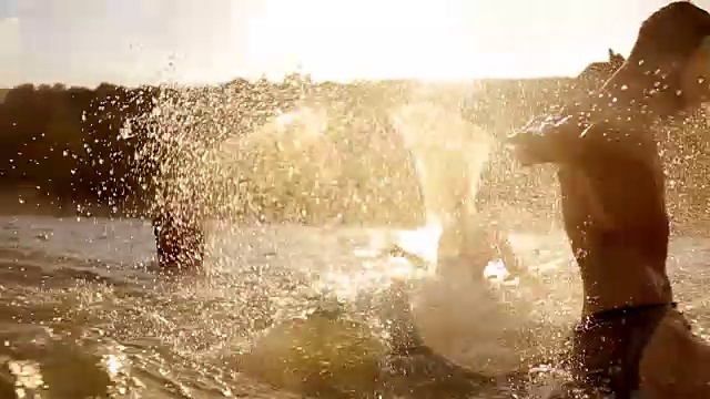 一群朋友在日落时在海里游泳，在慢动作中被淋湿和溅起水花。年轻人在水里玩视频素材