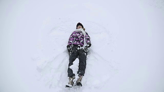 穿着冬季夹克的年轻女子正在做一个雪天使。视频下载