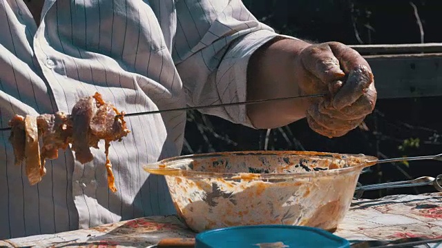 胖子把腌过的生肉串在烤肉串上视频素材