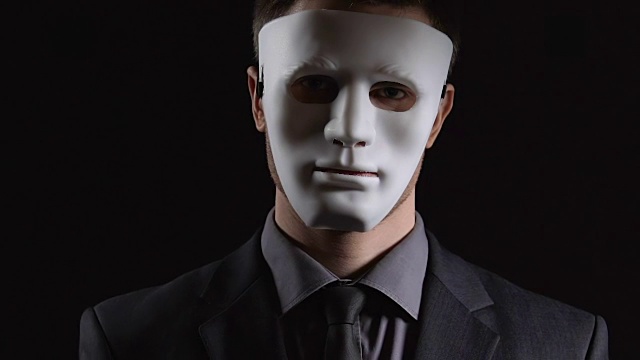 戴着面具的匿名西装男子双手合十在黑色背景下，非法活动视频下载