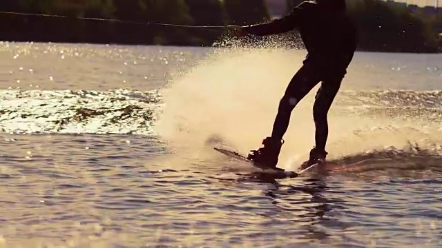 在金色的夕阳下，滑水板骑手在水花中快速移动视频素材