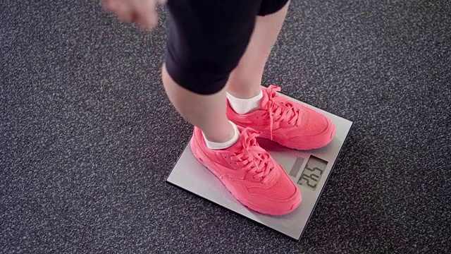 用电子秤秤体重的女孩。苗条的女性腿在粉色运动鞋在数字平衡视频素材