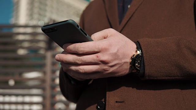 男性手握着手机打字的特写，白天在户外视频素材