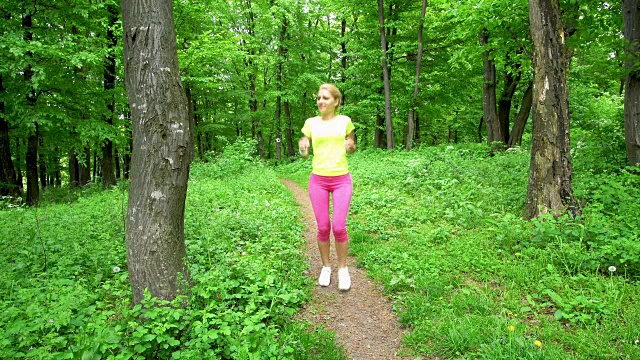 年轻的女运动员在森林里跑步时伸展双腿。视频素材