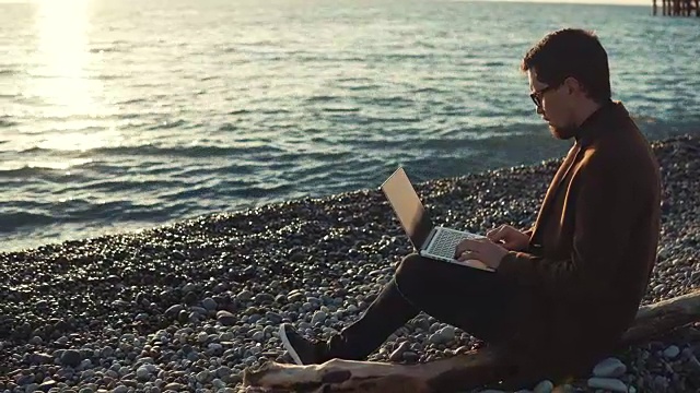 一个严肃的人正坐在沙滩上拿着笔记本电脑视频素材
