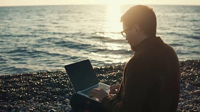 一个成年人在用笔记本电脑工作，一个商人坐在海边视频素材