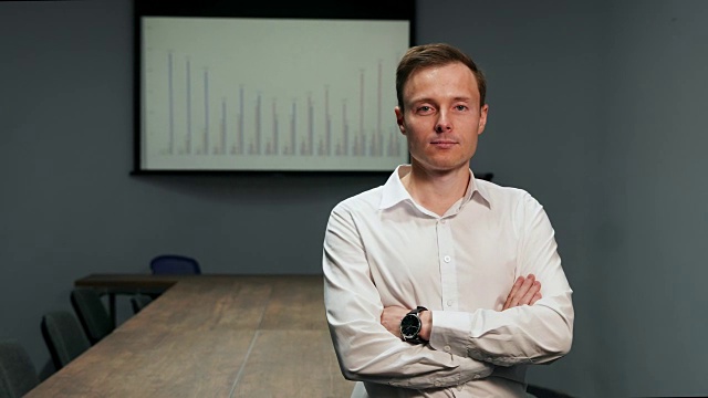 一个穿着白衬衫的男人站在办公室的肖像，在会议桌的背景上，投影仪上的图表图像视频素材