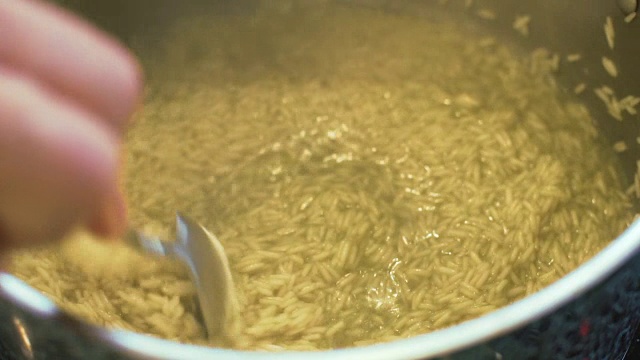 用勺子将米拌入开水中，放入不锈钢锅中，慢吞吞视频素材