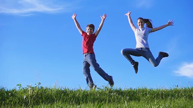 快乐的孩子们一起跳跃在绿色的草山上，对着蓝天视频素材