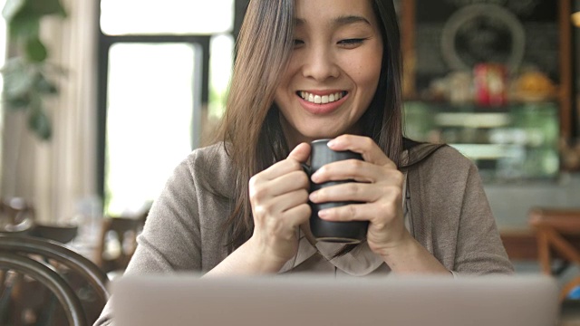 女人看笔记本电脑和咖啡在咖啡馆喝视频素材