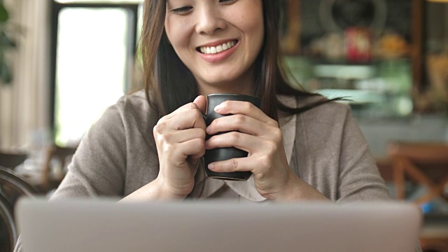 一个女人在咖啡馆边喝咖啡边看笔记本电脑视频素材