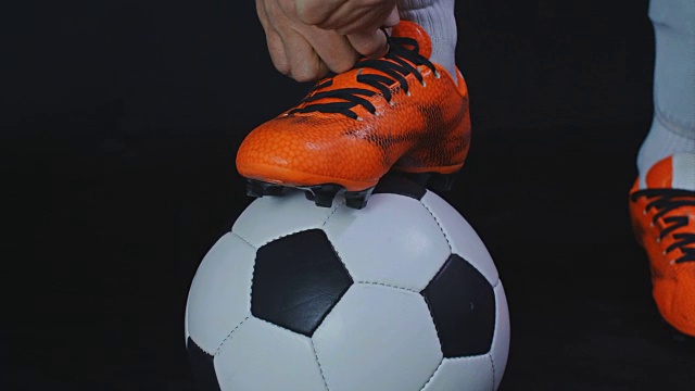 足球,足球比赛。职业足球运动员扣上他的红鞋，黑色背景视频下载