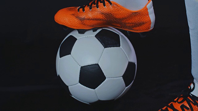 穿着靴子的足球运动员把他的腿放在一个球上，黑色的背景视频下载