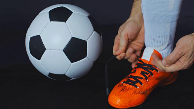 足球,足球比赛。职业足球运动员扣上他的红鞋，黑色背景视频下载