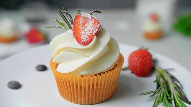 甜点厨师女手装饰美味的纸杯蛋糕白奶油顶部切草莓块在厨房视频下载