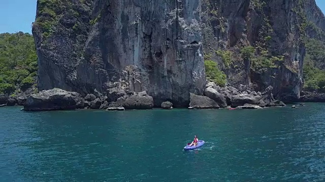 航拍:一名女性游客驾驶着她的皮划艇离开巨大的石灰岩岛屿。视频下载
