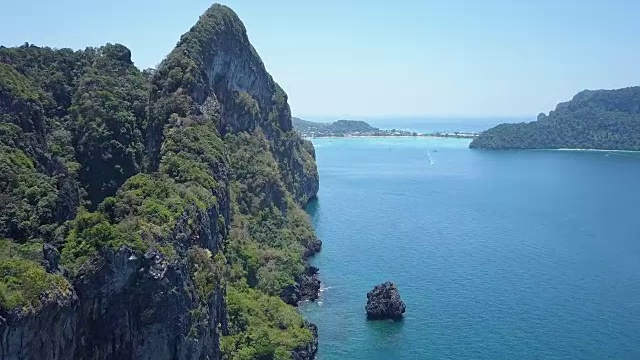 航拍:在阳光明媚的海滩附近，沿着覆盖着绿色植物的石灰岩悬崖飞行视频下载